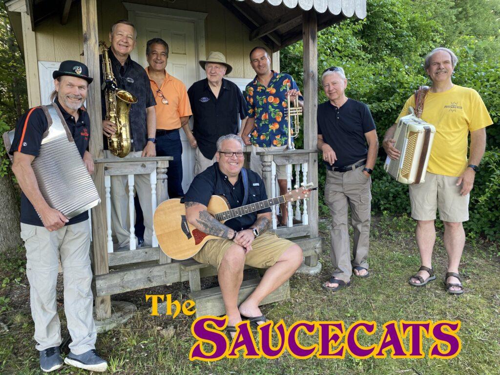 A band named The Saucescats posing with musical instruments outdoors.