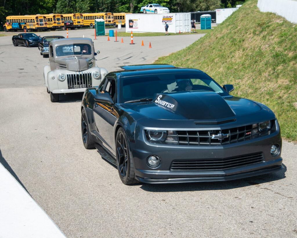 A black sports car leads a silver vintage car on a sunny road.