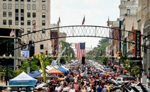 Crowded street festival with American flags and tents in an urban setting.