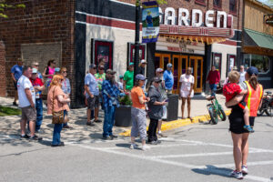 People gather on a street corner near a brick building with colorful murals.