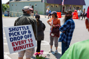 People gather near a shuttle pick-up and drop-off area with signage.