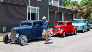 Two vintage cars parked outside a building with a man inspecting them.