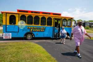 People walking near the Crystal Lake Express trolley on a sunny day.