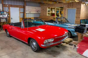 Classic red convertible car parked inside a rustic garage.
