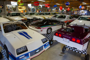 A collection of classic sports cars displayed indoors under colorful neon signs.