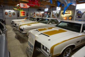 Classic white and gold muscle cars displayed in a vintage garage.