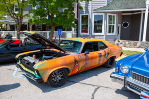 A bright orange vintage car with its hood open, showing a custom paint job and parked outdoors.