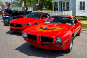 Two vibrant red muscle cars parked side by side on a sunny day.