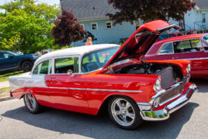 Classic red and white vintage car with hood open at a car show.