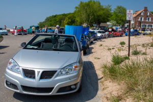 Line of cars waiting on a dirt road under a clear sky.