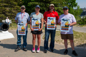 Four people stand outdoors holding colorful event posters.