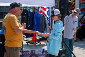 A young person hands out flyers at an outdoor event booth.