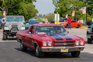 Classic red and black Chevrolet El Camino driving in a parade.