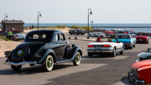 Classic and modern cars parked by the seaside under street lamps.
