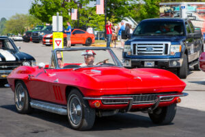 Red convertible sports car driving on a busy street with people and vehicles around.