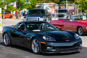 A sleek black Corvette parked outdoors with other vehicles around.