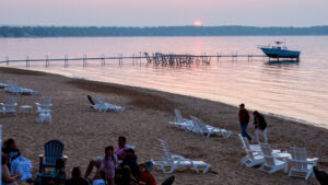 Sunset over a calm beach with scattered loungers and people relaxing.