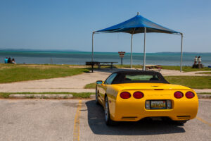 Yellow sports car parked near a beach with a blue canopy in the background.