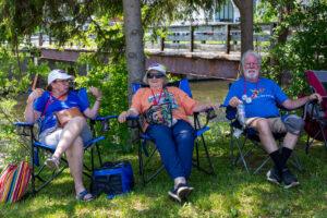 Three people relaxing on foldable chairs in a sunny park.