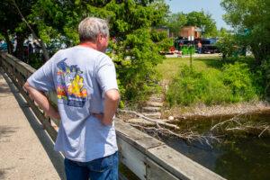 Man in casual wear looking at a river from a wooden bridge on a sunny day.