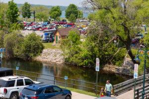 People near a crowded lakeside parking area with boats and trees.
