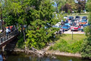 A scenic riverside park with lush trees and a parking area filled with cars.
