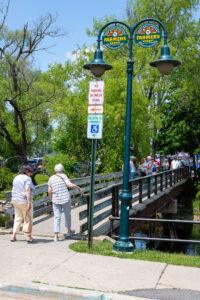 Two elderly women walk with canes toward a bridge on a sunny day.