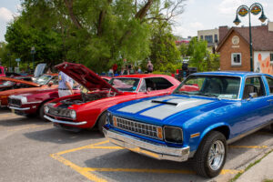 Classic muscle cars displayed at an outdoor car show with vibrant colors and open hoods.