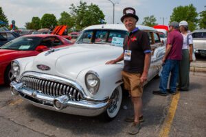 Man posing next to a vintage white Buick car at a car show.