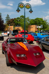 A red classic convertible with yellow racing stripes at a car show.