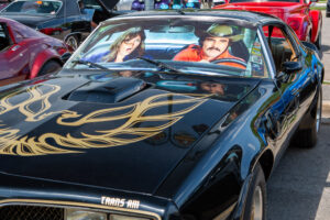 Couple posing in a classic black Pontiac Trans Am with gold detailing.