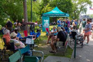 Community members gather outdoors for a group meeting under a branded canopy.