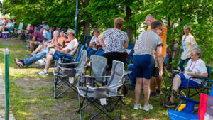 People gathered outdoors, sitting and standing around in a green park area.