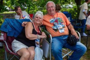 An elderly couple smiling and sitting outdoors on chairs.