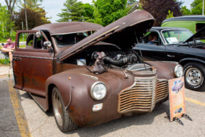 Rusty vintage car with its hood open at an outdoor show.