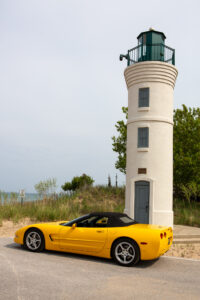 Yellow convertible sports car parked near a white lighthouse by the sea.