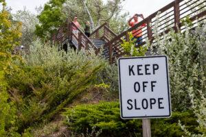 A 'Keep Off Slope' sign near a slope with people on a stairway above.