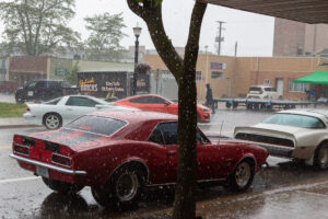 Classic red car parked on a rainy day beside a tree.