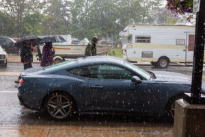 A black sports car parked on a snowy street with people and vehicles in the background.
