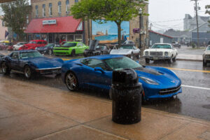 Blue sports car parked on a rainy urban street with other vehicles nearby.