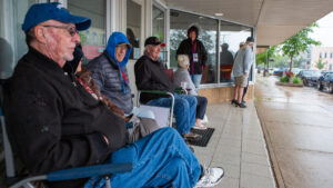 People sitting and standing on a covered porch on a cloudy day.
