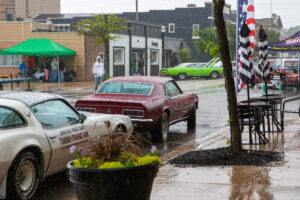 Vintage cars parked on a rainy street with puddles and reflections.