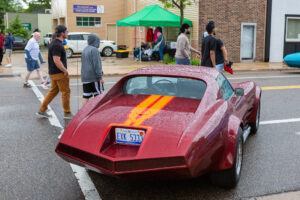 Custom red car with yellow stripes parked on city street with people nearby.
