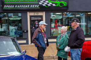 Three elderly people chat outside a model hobby shop.
