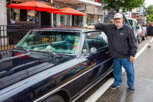 Man posing next to a vintage black car on a street.