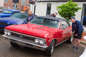 A red classic Chevrolet car parked outdoors with two people nearby.