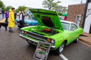 Bright green vintage muscle car with its hood open at a car show.