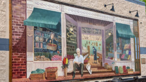 A man and dog sitting in front of a colorful bookstore mural on a wall.