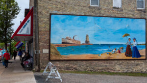 Mural of a ship and lighthouse on a seaside wall.