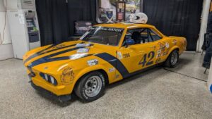 A vintage yellow race car with black stripes and number 42 on display.